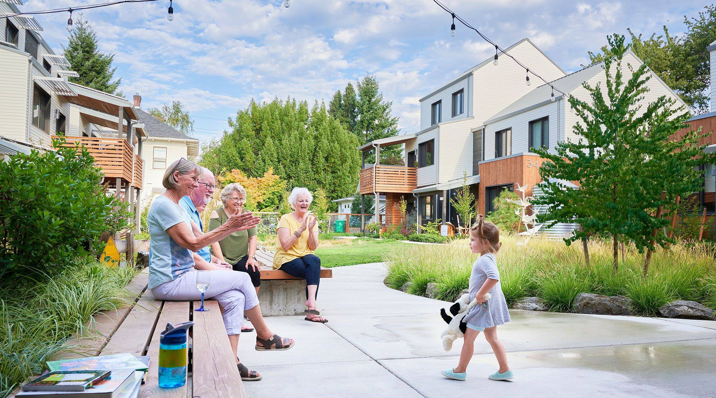 Residents seated on bench and greeting little girl in central courtyard at Tillamook Row in Portland, Oregon.