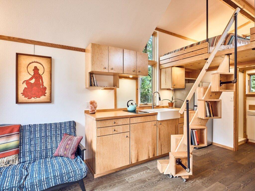 Interior of tiny house barnraising project showcasing kitchen, seating area, and staircase with storage boxes.
