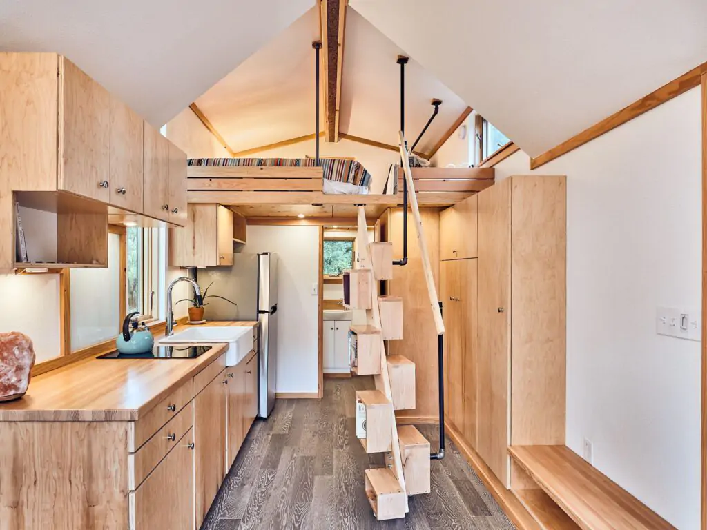 Interior of tiny house barnraising project with kitchen, staircase, loft, and storage cabinets space.