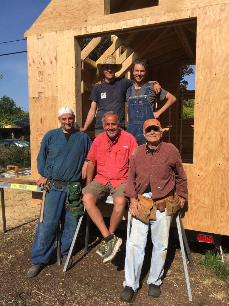 Five volunteers from Buddha Eye temple community posing in front of frame of tiny house barnraising project.